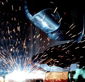 Person in welding helmet leaning over a sparking weld