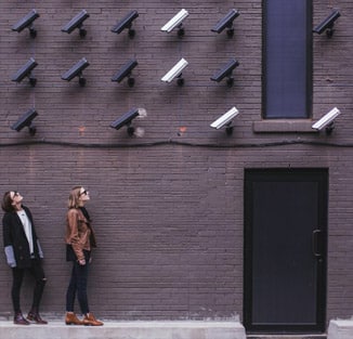 Two people on an urban street, looking up at, not one, but several security cameras looking at them from above a door